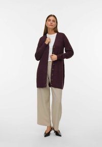 Cardigan en tricot bordeaux avec un col en V, des manches longues et six boutons marron. Associé à un pantalon large beige et des talons noirs.