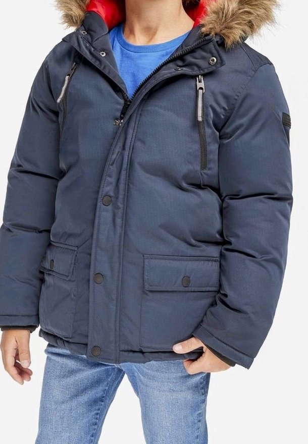 Personne portant une veste d'hiver bleu marine avec une capuche doublée de fourrure, zippée et boutonnée, associée à un jean bleu clair.