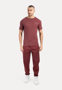 Weinrotes Sportshirt mit kurzen Ärmeln und dazu passenden Jogginghosen. Hergestellt aus weichem Stoff, mit engem Schnitt und weißen Turnschuhen.