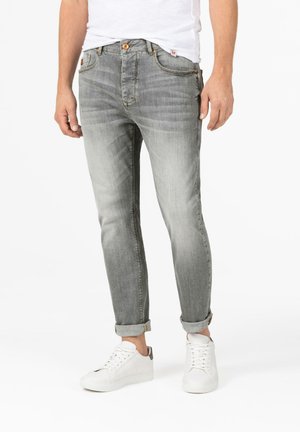 Light gray denim jeans with a tapered fit, featuring a classic five-pocket design, distressed texture, and rolled cuffs, paired with white sneakers.