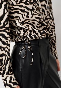 Zwart-witte blouse met zebra-strepen en textuurstof, op de taille geknoopt, gecombineerd met strakke zwarte leren broek.