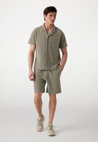Maglietta a maniche corte verde chiaro a righe e pantaloni corti abbinati. Vestibilità casual con bottoni al colletto; abbinata a sneakers beige.