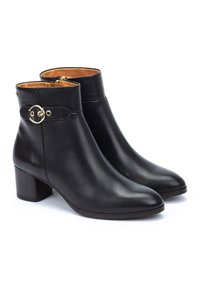 Bottines en cuir noir avec un bout arrondi et un talon épais. Elles présentent une sangle avec une boucle dorée circulaire sur le côté.