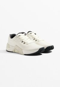 Białe buty sportowe z teksturowaną dzianinową cholewką, czarnymi akcentami na kołnierzu oraz gumową podeszwą zewnętrzną z wzorem jodełki.