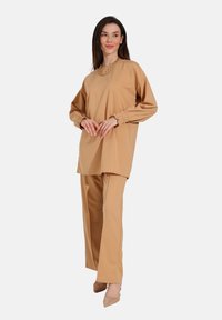 Beige top og bukser sæt i glat stof; toppen har puffede ærmer og en rund halsudskæring, parret med lige bukser.