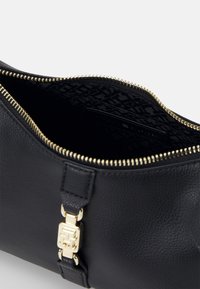Černá kožená taška s texturovaným povrchem, zlatým zipem a doplňky. Interiér má vzorovanou černou podšívku a štítek s logem.