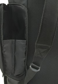 Sac en mesh noir avec une poche zippée et une sangle ajustable. Le matériau texturé permet une respirabilité et une flexibilité dans le design.