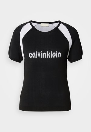 Black knitted short-sleeve top with white raglan sleeves. Features "calvinklein" text in white across the chest. Round neckline. Soft texture.