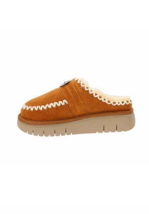 Scarpa slip-on in suede tan con cuciture bianche, interno morbido e suola spessa in gomma beige. Presenta dettagli decorativi sul lato.