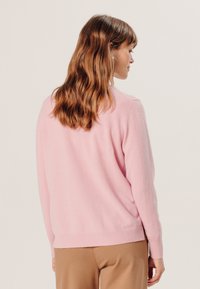 Rosa gestrickter Pullover mit Rundhalsausschnitt und geripptem Saum. Die Rückseite zeigt eine lockere Passform und eine weiche Textur, die sich gut zum Überziehen eignet.