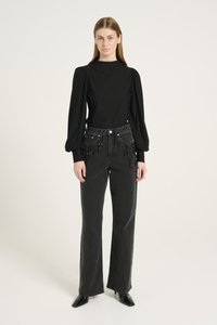 Black long-sleeve top with puffed shoulders paired with black jeans featuring bead accents along the pockets and straight legs, finished with pointed shoes.