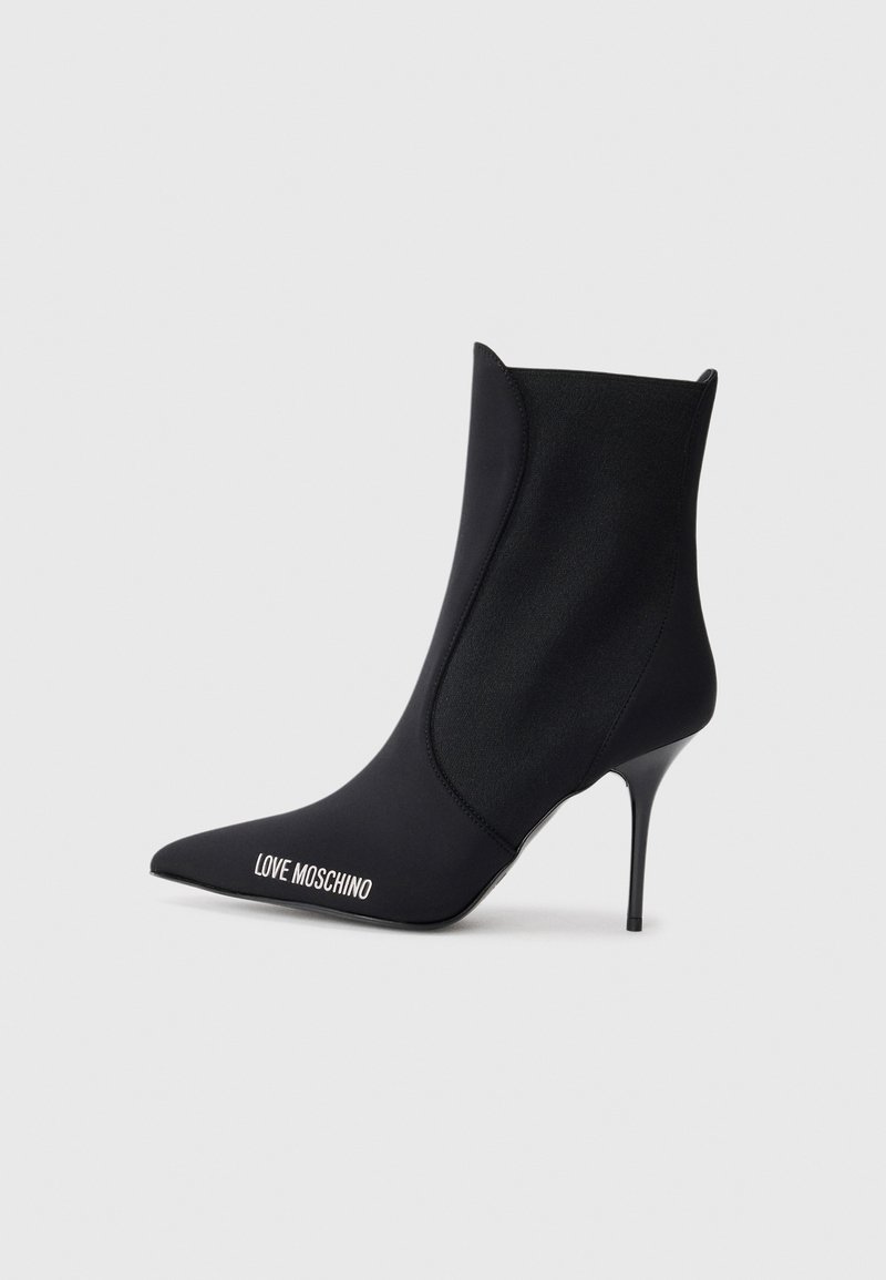 Bota ankle preta com bico fino, feita de um material suave, apresentando um alto salto agulha e o logótipo "LOVE MOSCHINO" em branco.