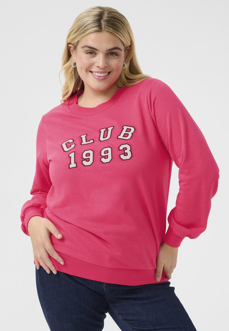Vaaleanpunainen huppari, jossa on valkoisella ja harmaalla brodattu "CLUB 1993", klassinen pyöreä kaula-aukko ja ribatut hihansuut sekä helma.