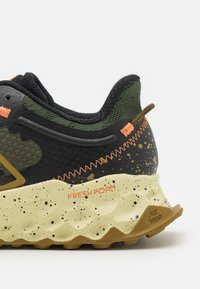 Black and olive green sneaker featuring a textured mesh upper, orange accents, speckled midsole, and rugged sole with "FRESH FOAM" branding.