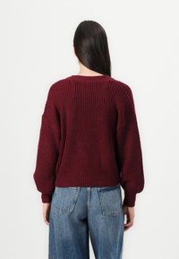 Bordeaux gebreide trui met een ontspannen fit, geribbelde textuur en ballonmouwen. Gecombineerd met lichtblauwe wijde jeans.