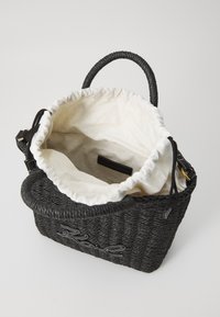 Crna pletena torba s okruglim ručkama, s kremastom unutrašnjošću, zatvaranjem na vezicu i izvezenim detaljima. Ima meki, teksturirani interijer.