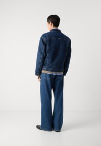 Mörkblå denimjacka med krage, matchad med löst sittande mörkblå jeans. Tyget verkar vara robust, med standard bakfickor.