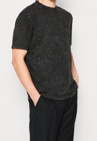 Svart kortärmad T-shirt med marmorering, rund halsringning och avslappnad passform. Tillsammans med svarta byxor.