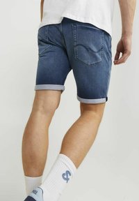 Shorts in denim con orlo arrotolato, lavaggio scuro, due tasche posteriori, semplice dettaglio di cucitura, abbinati a calzini bianchi e scarpe blu.