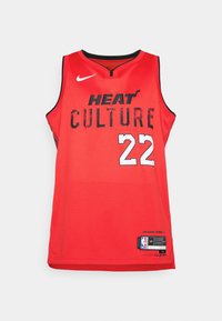Camiseta de baloncesto roja con "HEAT CULTURE" en negro y el número "22" en blanco. Logo de Nike en el hombro izquierdo. Textura de tela de malla.