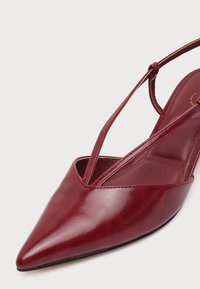 Chaussure slingback en cuir rouge à bout pointu avec des fines lanières sur un fond clair uni.