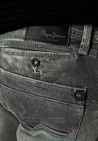 Grå denimjeans med en strukturerad yta, med en svart läderetikett, knappdetalj på bakfickorna och kontrasterande sömmar.