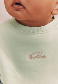 Sweatshirt vert menthe avec col côtelé, présentant un texte brodé rose "LITTLE" près de l'encolure. Texture douce du tissu.