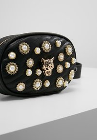 Borsa a cintura in pelle nera trapuntata con borchie dorate e perle, e un ornamento centrale a testa di leopardo dorato.
