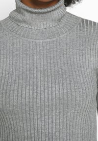 Maglione grigio a collo alto con coste, caratterizzato da un collo alto e un tessuto testurizzato, che mette in evidenza linee verticali in un design aderente.
