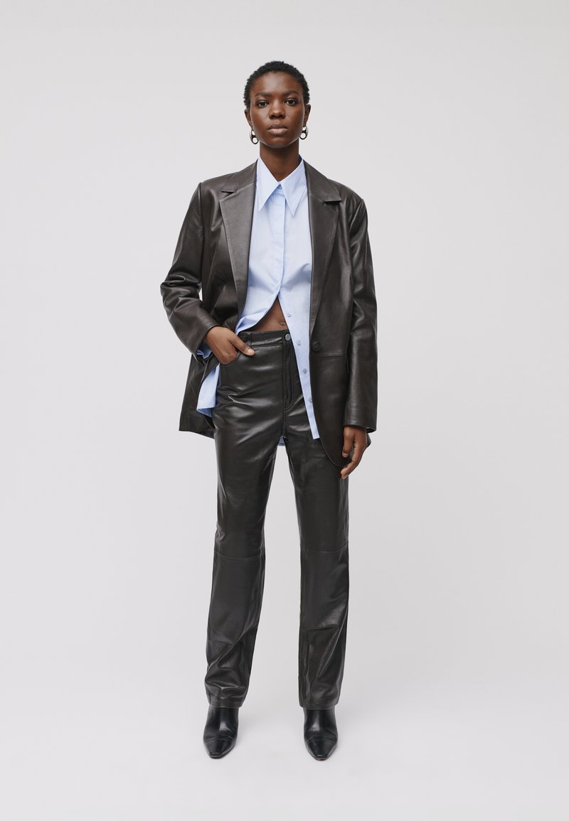 Blazer e pantaloni in pelle nera abbinati a una camicia azzurro chiaro, con design a bottoni e silhouette slanciata e attillata.