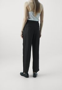 Svarta linnebyxor med rak passform, som har bakfickor och midjeband, kombinerat med en ljus linne-topp och svarta skor.