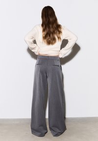 Pantalon gris à jambes larges avec une finition texturée et deux poches arrière, associé à un pull ajusté de couleur crème.
