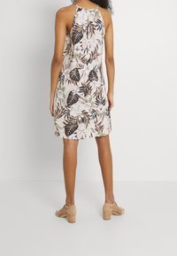 Sukienka w kwiatowy wzór na różowym tle, z czarnymi i zielonymi liśćmi oraz białymi kwiatami. Wzór na szyjkę bez ramiączek i luźny krój.