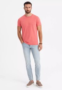 Tričko s krátkým rukávem v korálové barvě, kombinované s světle modrými džínami a béžovými slip-on botami, s uvolněným střihem a klasickým kulatým výstřihem.