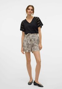 Top negro con detalles de encaje, combinado con pantalones cortos beige con un estampado geométrico. La modelo lleva bailarinas negras y tiene el cabello largo y castaño.