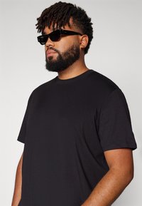 Schwarzes Baumwoll-T-Shirt mit kurzen Ärmeln, ergänzt durch kantige schwarze Sonnenbrillen. Der Stoff wirkt weich und hat eine normale Passform.