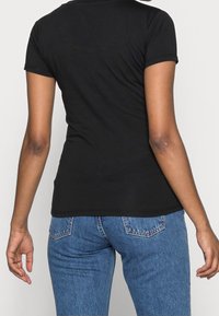 Svart, figurnära t-shirt med korta ärmar, tillverkad av ett mjukt material. Matchad med högmidjade, ljusblå denimjeans.