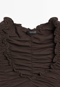 Tissu froncé marron foncé avec des bords volantés et une étiquette "Massimo Dutti Made in Morocco" cousue au centre en haut.