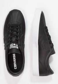 Baskets basses en cuir noir de Converse avec des semelles en caoutchouc blanc, logo en étoile sur les côtés, lacets noirs et semelles intérieures à logo.