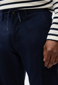 Mørkeblå bomuldsbukser med tekstureret finish, udstyret med snøre i taljen, sidelommer og en langærmet skjorte med kontrasterende striber.