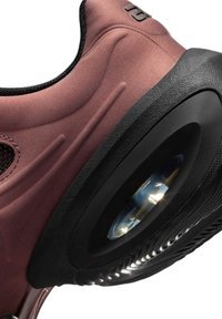 Nahaufnahme der Ferse eines kastanienbraunen Sneakers mit schwarzer Außensohle, die eine sichtbare Luftpolstereinheit und ein strukturiertes Griffmuster zeigt.