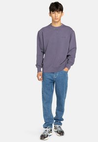 Purple sweatshirt with a crew neck, ribbed cuffs, and stitching details, paired with light blue straight-leg jeans and multi-colored sneakers.