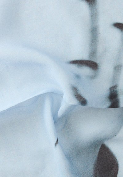 Gros plan d'un tissu bleu clair avec des formes abstraites gris foncé et des plis doux créant une texture lisse.