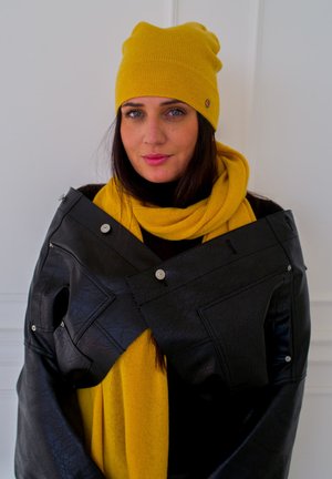 Black faux leather jacket with silver hardware, paired with a bright yellow knit beanie and matching scarf. Smooth texture, contemporary design.