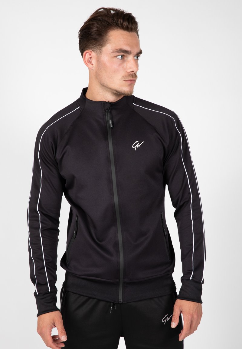 Zwarte sportjack met hoge kraag, ritssluiting en witte zijstrepen. Heeft ritszakken en geribbelde manchetten.