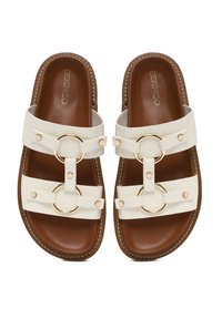 Weiße Sandalen mit zwei Riemen und großen Metallringen. Braunes, gepolstertes Fußbett mit genähten Details und dekorativen Nieten.