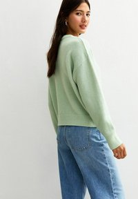 Maglione verde menta con una vestibilità comoda e orlo a coste, abbinato a jeans a vita alta blu chiaro. Texture simile alla lana, maniche risvoltabili.