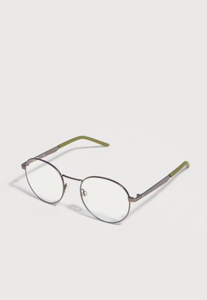 Lunettes rondes à monture métallique avec des cercles argentés fins et des embouts de branches vert olive, posées sur une surface blanche.