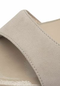 Beige suede slide sandal with a crossover upper design, smooth texture, and minimal stitching detail along the edges.