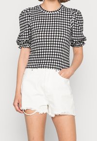 Top a maniche puff in gingham bianco e nero abbinato a pantaloni corti di denim bianco strappati. Il top presenta un collo rotondo e un tessuto strutturato.